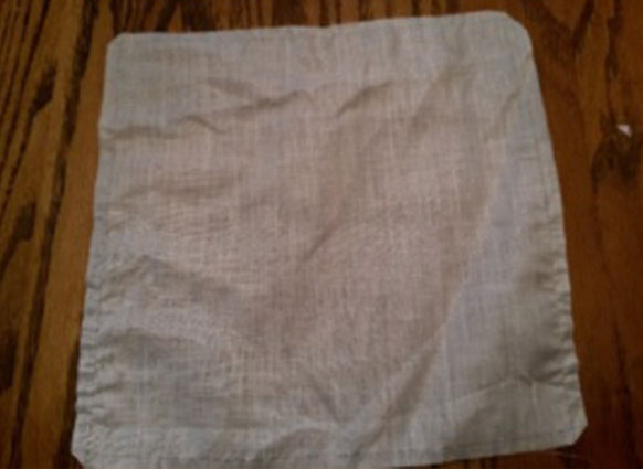 Photo shows a 12 inch square of handkerchief weight 100 5% linen with the corners clipped and a line along the four edges 1/4 inch from the edge, where a single thread is pulled out. The missing thread shows a line that is followed to crochet a lace border onto the fabric, after the edge is rolled to the line.